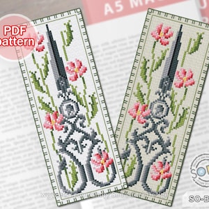 Pode incluir: Padrão de marcador de ponto cruz com um par de tesouras com detalhes florais. O padrão é em preto e branco com flores cor-de-rosa e folhas verdes. O padrão é etiquetado como "SO-BM73".