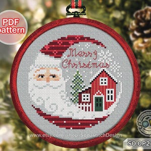 May include: A cross-stitch Christmas ornament featuring Santa Claus, a red house, and a green Christmas tree. The words "Merry Christmas" are stitched in white. The ornament is framed in a red hoop with a green and red striped ribbon.