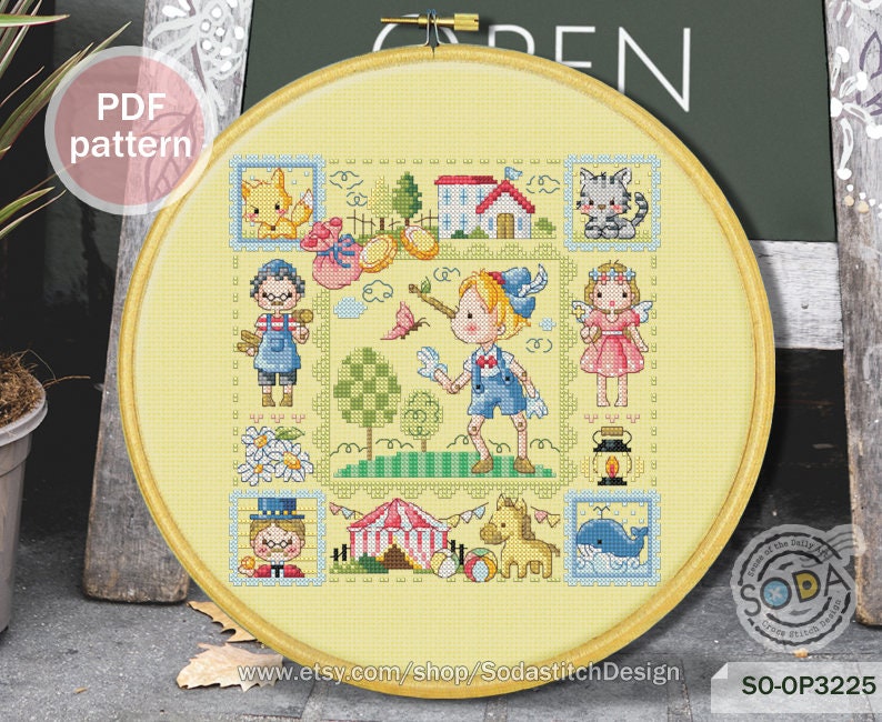 May include: A colorful cross-stitch pattern featuring a whimsical scene with children, animals, and a circus tent. The pattern is framed in a yellow hoop and includes the text "SO-OP3225".