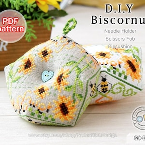 Può includere: Due cuscini biscornu fatti a mano con motivi a punto croce di girasoli. Uno ha un bottone blu a forma di cuore. Il testo sull'immagine dice "D.I.Y Biscornu" e "Needle Holder, Scissors Fob, Pincushion".