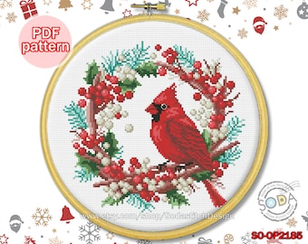 May include: A cross stitch pattern featuring a red cardinal perched on a winter wreath with red berries and green pine branches. The pattern is available as a PDF download. The text "SO-OP2185" is in the bottom right corner of the image.