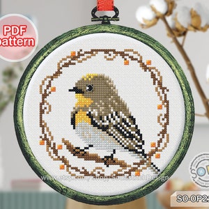 May include: Cross stitch pattern of a yellow and brown bird perched on a branch with a wreath of brown vines and orange berries. The pattern is in a round embroidery hoop with a green wooden frame. The pattern is labeled "SO-OP2194".