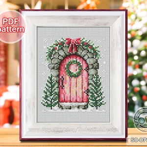 May include: Cross-stitch pattern of a pink door with a wreath, framed in a white and red border. The door is surrounded by greenery and stone, with a red bow at the top. The text "PDF pattern" is in the upper left corner.