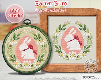 May include: A cross-stitch pattern featuring a white bunny in a pink egg surrounded by white flowers and green leaves. The pattern is 60 x 60 stitches and is available as a PDF download. The pattern is titled "Easter Bunny".