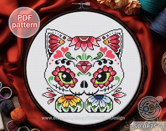 May include: Cross-stitch pattern of a white cat with a sugar skull design. The cat has pink, red, and green flowers on its head and a large diamond on its forehead. The cat's eyes are green and its paws are decorated with flowers.