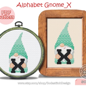Puede incluir: Un patrón de punto de cruz con un gnomo verde sosteniendo la letra X. El patrón está en un marco de madera y está etiquetado como "Alphabet Gnome_X" y "SO-X".