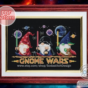 May include: Cross-stitch pattern featuring three gnomes dressed as Star Wars characters. The gnomes are standing in front of a space background with stars and planets. The text "Gnome Wars" is written in yellow letters with a red outline. The website address "www.etsy.com/shop/SodastitchDesign" is written below the text.