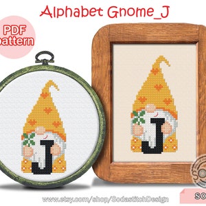 Peut inclure: Un modèle de point de croix représentant un gnome tenant la lettre J. Le gnome porte un chapeau jaune à pois orange et a une barbe blanche. La lettre J est noire. Le motif est dans un cadre en bois avec un fond blanc. Le texte "Alphabet Gnome_J" est en haut de l'image. Le texte "PDF pattern" est dans un cercle rose en haut à gauche de l'image. Le texte "SO-J" est en bas à droite de l'image.