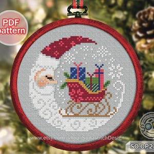 May include: A cross-stitch Christmas ornament featuring Santa Claus with a red hat and a sleigh filled with gifts. The design is set within a red circular frame, with the text "PDF pattern" visible.