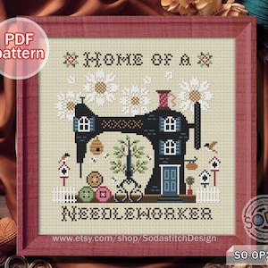May include: Cross-stitch pattern framed in a red wooden frame. The design features a black sewing machine with a house-like structure, the text "HOME OF A NEEDLEWORKER", and decorative elements like flowers, birds, and a beehive.