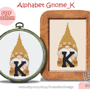 Op de afbeelding: Een kruissteekpatroon voor een kabouter die de letter K vasthoudt. De kabouter draagt ​​een bruine hoed en heeft een witte baard. Het patroon is in een houten frame en bevat de tekst "Alphabet Gnome_K" en "SO-K".