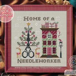 May include: Cross-stitch pattern framed in a red wooden frame. The design features a Christmas tree with scissors, a house with gifts, and the text "HOME OF A NEEDLEWORKER". The color palette includes red, green, and brown.