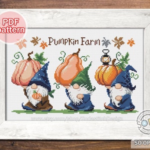 May include: Cross-stitch pattern showing three gnomes with pumpkins, with the words "PUMPKIN FARM." The gnomes wear blue and green hats and carry orange and peach pumpkins. The design is framed in a white wooden frame.