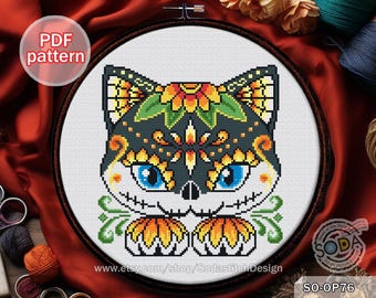 May include: Cross stitch pattern of a black cat with a sugar skull design. The cat has yellow and orange flowers on its head and a white background. The pattern is called "SO-OP76".