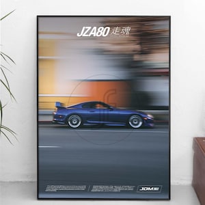 May include: A framed poster featuring a motion-blurred side view of a dark blue JZA80 sports car driving on a road. The text JZA80 and Japanese characters appear at the top, with additional small text and a JDM logo at the bottom of the print.