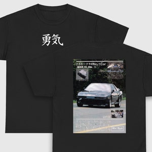 May include: Black t-shirt with Japanese text "勇気" on the front and a black and white magazine clipping on the back featuring a black Toyota Supra with the text "2.5スープラのNo.1 Car [最高速]305.89km/h" and "Mid Night".