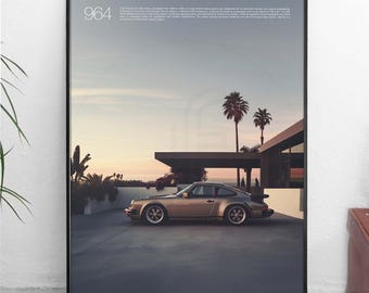 May include: A poster with a black frame featuring a gold Porsche 964 driving on a paved road in front of a modern house with palm trees. The poster has the text "964" in the top left corner and "Designed by Arthur Fulford" in the bottom left corner.