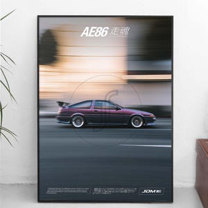 Op de afbeelding: Een ingelijste poster met een paarse AE86-auto in beweging tegen een wazige achtergrond. De tekst AE86 走魂 staat bovenaan en kleinere tekst met het JDM-logo onderaan. De auto heeft een achterspoiler en zilverkleurige wielen.