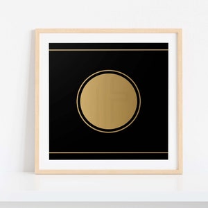 May include: A framed art print featuring a black background with a gold circle in the center. Gold horizontal lines are above and below the circle. The frame is light wood.