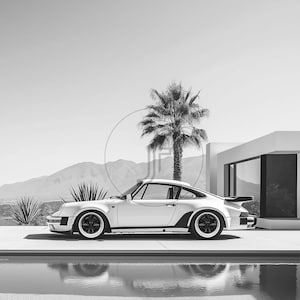 May include: A silver Porsche 930 Turbo sports car parked in front of a modern house with a palm tree in the background. The car is parked on a concrete driveway next to a swimming pool.