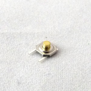 Peut inclure: Un petit bouton poussoir rond de couleur dorée avec deux fils argentés.