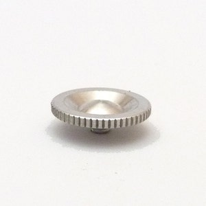 May include: A circular silver-toned metal knob featuring a concave center and a textured, knurled edge for grip. The component has a small, centered protrusion on the underside, designed for mechanical attachment or adjustment in various hardware applications.