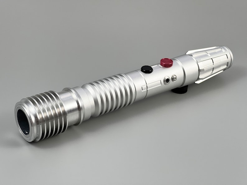 Puede incluir: Una r&eacute;plica de sable l&aacute;ser plateado con un agarre texturizado, botones negros y rojos y un soporte de hoja plateado.