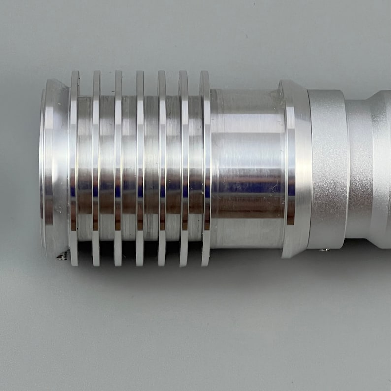 Puede incluir: Una extensi&oacute;n de sable de luz de metal plateado con una serie de anillos o ranuras a lo largo de la extensi&oacute;n.