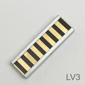 Peut inclure: Un fermo &agrave; cravate en m&eacute;tal ray&eacute; argent et noir. Le fermoir &agrave; cravate a une finition argent&eacute;e et des rayures noires.