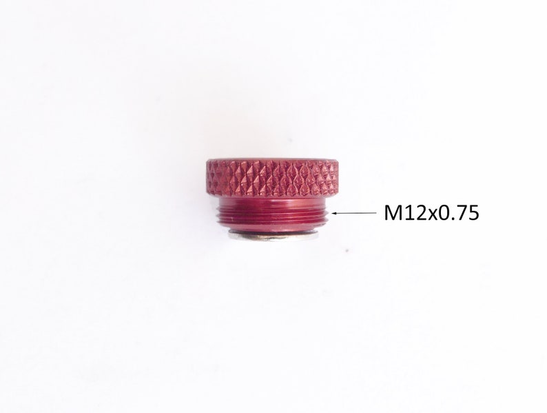 May include: A maroon-colored metal component with a textured top and threaded base. The text "M12x0.75" is printed on the side, indicating the size and thread pitch of the component. The object is set against a white background.