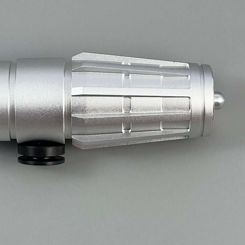 Puede incluir: Una empu&ntilde;adura de sable de luz de metal plateado con un dise&ntilde;o texturizado y estriado. La empu&ntilde;adura tiene una empu&ntilde;adura de goma negra y una punta plateada.