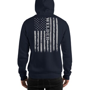 May include: Navy blue hooded sweatshirt with a distressed American flag design on the back. The flag is gray and white with the word "WELDER" vertically down the right side.