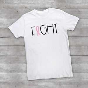 May include: White t-shirt with the word "FIGHT" in black text and a pink ribbon graphic.