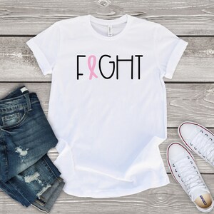 May include: White t-shirt with the word "FIGHT" in black letters and a pink ribbon in the middle of the word.