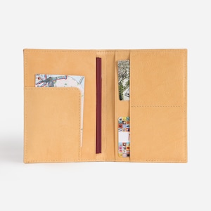 May include: A tan leather passport holder with multiple pockets for cards and documents. The holder is open and shows a passport and several cards inside.