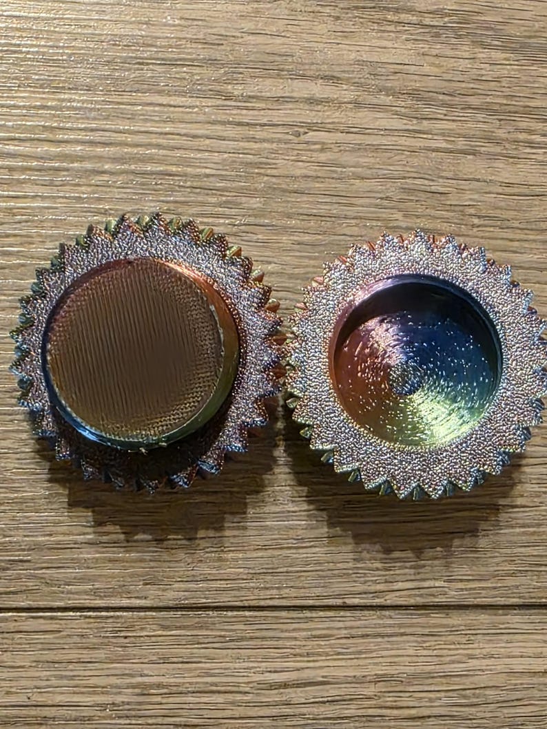 May include: Two iridescent, circular objects with a textured, ridged surface and a central, concave area. The objects have a metallic sheen with colors shifting from blue to green to purple. The outer edges are lined with small, pointed details.