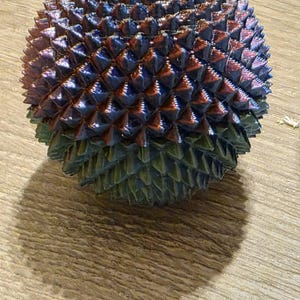 May include: A spherical object with a textured surface, featuring a pattern of small, pointed protrusions. The color transitions from a deep blue at the top to a green hue at the base, with hints of red and purple throughout.