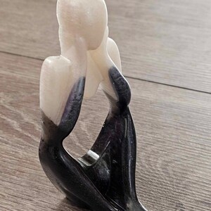 May include: A white and black abstract sculpture of a person sitting with their head in their hands.