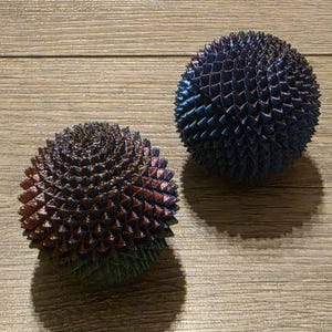 May include: Two spherical, spiky decorative objects. One is a mix of red, blue, and green hues, while the other is primarily blue with hints of purple. Both sit on a wooden surface, casting shadows.