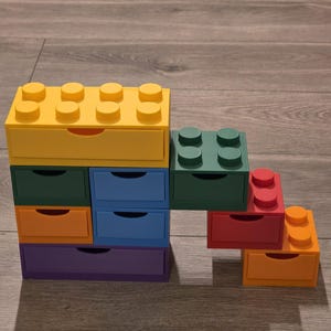 May include: A set of brightly coloured, stackable storage drawers designed to look like large toy building blocks. The drawers are in yellow, green, blue, orange, red, and purple. Each drawer has a pull-out design.