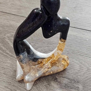 May include: A black and gold resin sculpture of a person sitting with their head resting on their hand. The sculpture has a modern abstract style.
