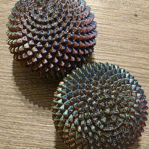 May include: Two iridescent, spherical objects with a textured, spiky surface. The spheres have a color gradient of blues, greens, and reds. The objects are resting on a light brown wooden surface.