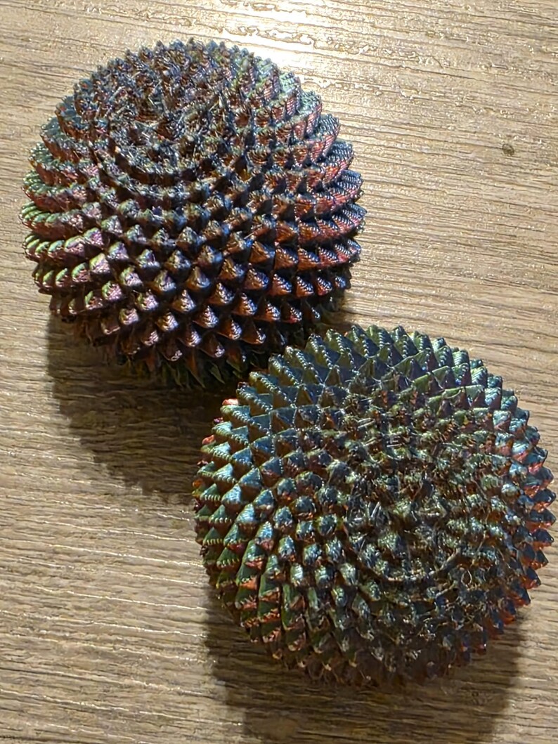 May include: Two iridescent, spherical objects with a textured, spiky surface. The spheres have a color gradient of blues, greens, and reds. The objects are resting on a light brown wooden surface.