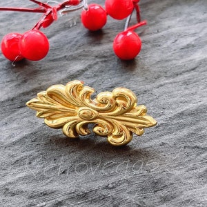 Puede incluir: Una pieza de metal decorativa de color dorado con un diseño floral. La pieza es adornada y tiene un diseño detallado.