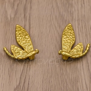 May include: Two gold-toned dragonfly drawer pulls with intricate wing details.