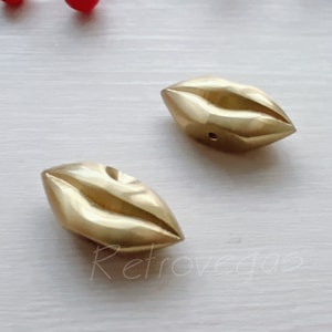 以下が含まれることがあります： 金色の金属製の唇の形をしたチャームペンダント2個。ペンダントは唇の形をしていて、ネックレスやブレスレットに取り付けるための穴が中央にあります。