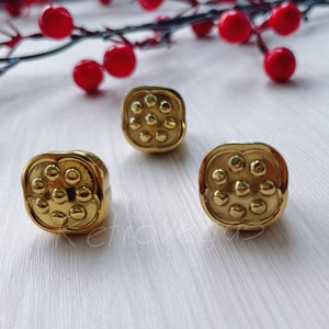 May include: Three gold-toned metal rings with a circular design featuring multiple raised dots. The rings are arranged on a white surface.