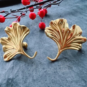 Peut inclure: Deux crochets en forme de feuille de ginkgo de couleur or. Les crochets sont décoratifs et ont une finition lisse et brillante.