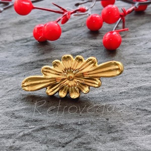 Op de afbeelding: Gouden decoratieve ladegreep met een bloemmotief. De greep heeft een licht gebogen vorm en een verhoogd midden.