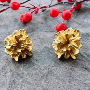 May include: A pair of gold-colored earrings shaped like a flower with a textured surface.